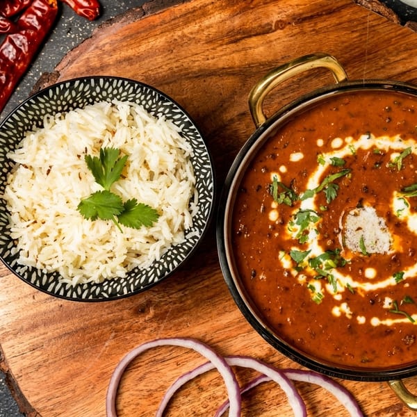 A bowl of white rice with cilantro and a pot of creamy dal makhani on a wooden board.