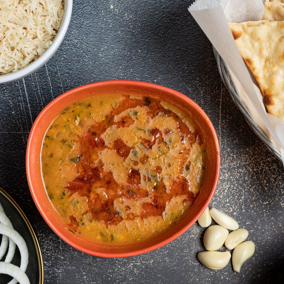 Overhead view of a bowl of dal, rice, naan, sliced onions, garlic cloves, and turmeric powder.