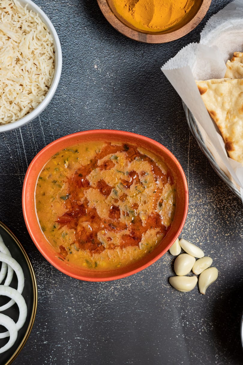 Overhead view of a bowl of dal, rice, naan, sliced onions, garlic cloves, and turmeric powder.