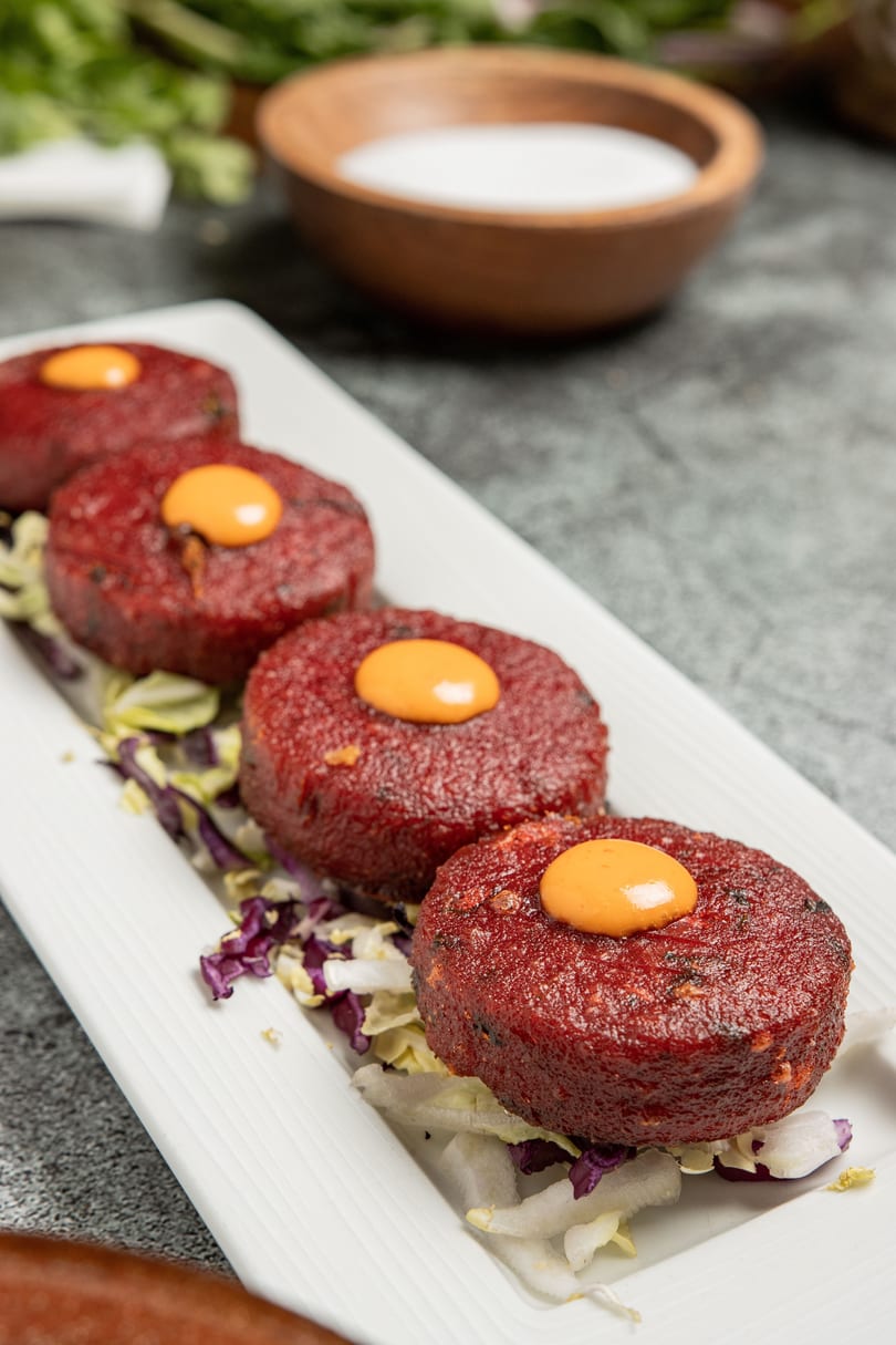 Four round, red patties with a dollop of orange sauce on top, served on a bed of lettuce.
