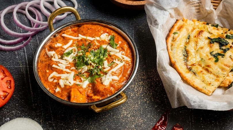 Indian butter chicken or paneer in a copper pot with naan bread, onions, and tomatoes.