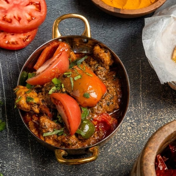 Indian curry with tomatoes and cilantro in a brass pot, with naan bread and spices.